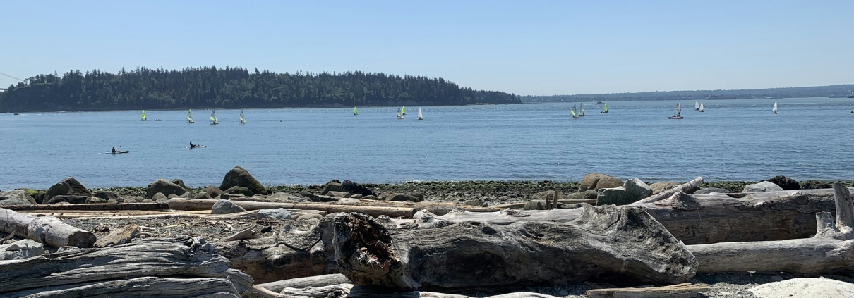 Sailing boats off a beach strewn with driftwood logs at Ambleside, West Vancouver.