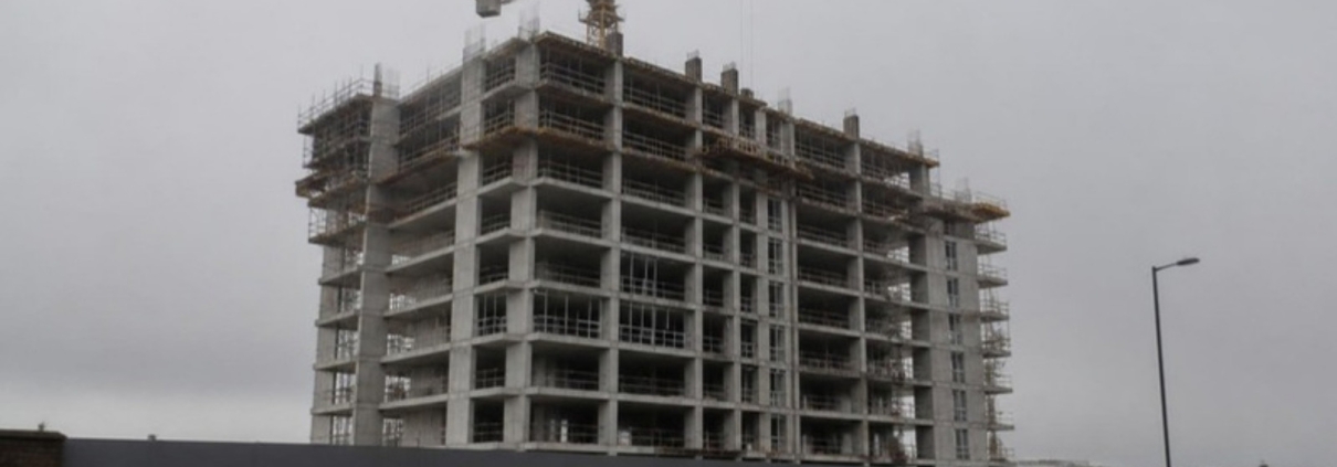 A residential tower under construction with a crane, seen from street level.