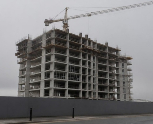 A residential tower under construction with a crane, seen from street level.