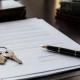 A signed document and house keys on a notary's desk with a pen.