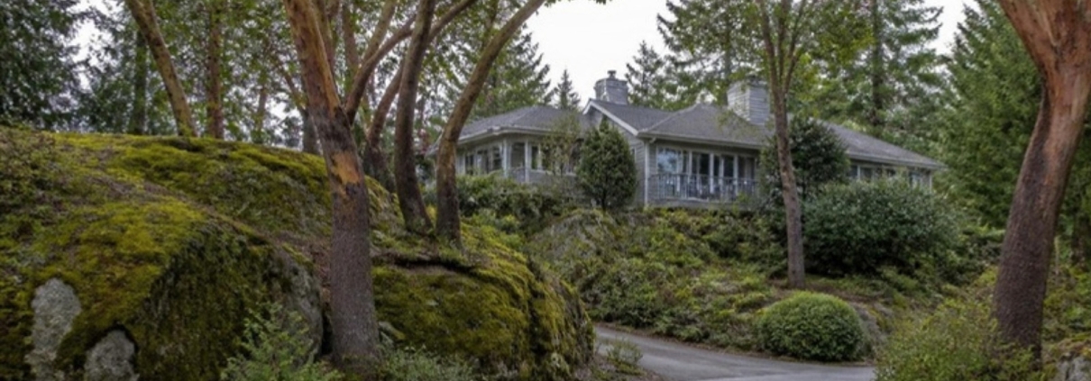 A large house set among arbutus trees and mossy rock outcrops on a winding lane.