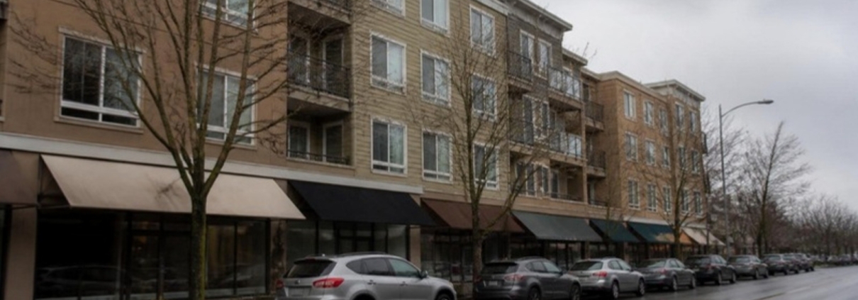 Apartment blocks above small shopfronts on a wet residential high street.
