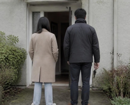 Two people seen from behind at the open front door of a townhouse.