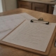 A clipboard with a handwritten list and a pen on a kitchen table.