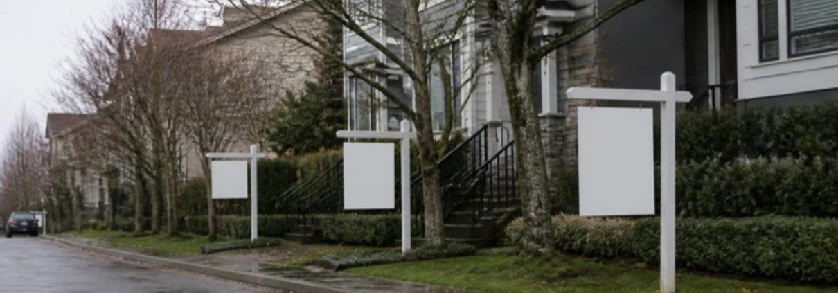 Blank real estate sign posts outside townhouses on a wet autumn street.
