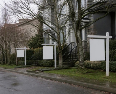 Blank real estate sign posts outside townhouses on a wet autumn street.