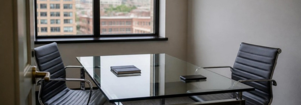 A small meeting room with a glass table, two empty chairs and a notebook.
