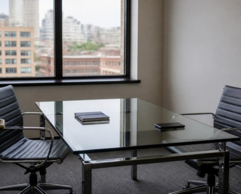 A small meeting room with a glass table, two empty chairs and a notebook.