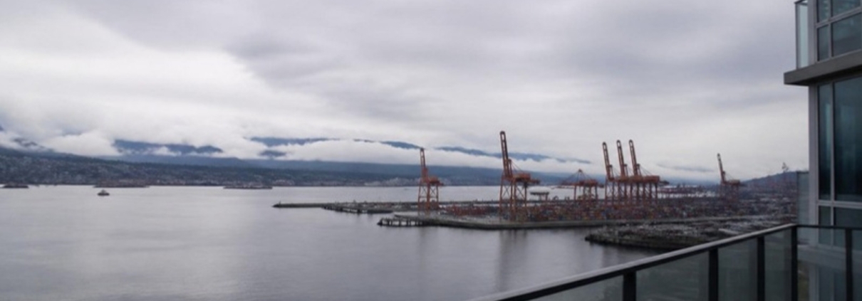 A residential balcony overlooking a working waterfront with distant cranes.