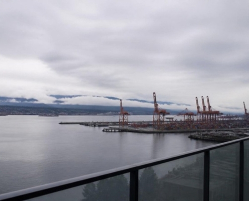 A residential balcony overlooking a working waterfront with distant cranes.