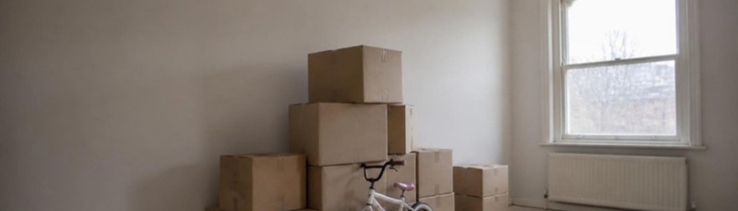 Moving boxes in an empty living room with a child's bicycle beside them.