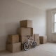 Moving boxes in an empty living room with a child's bicycle beside them.