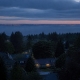 A residential hillside of detached houses and treetops at dusk.