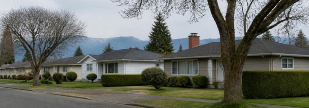Single-storey bungalows on a flat residential street with mountains behind.
