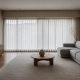 An empty staged living room with neutral furniture and sheer curtains.