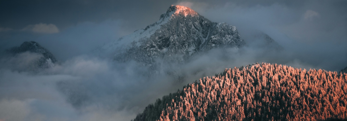Cloud breaking over a forested coastal mountain ridge at dusk.