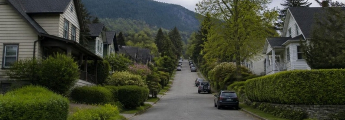 Older houses on a steep street climbing toward forested mountains.